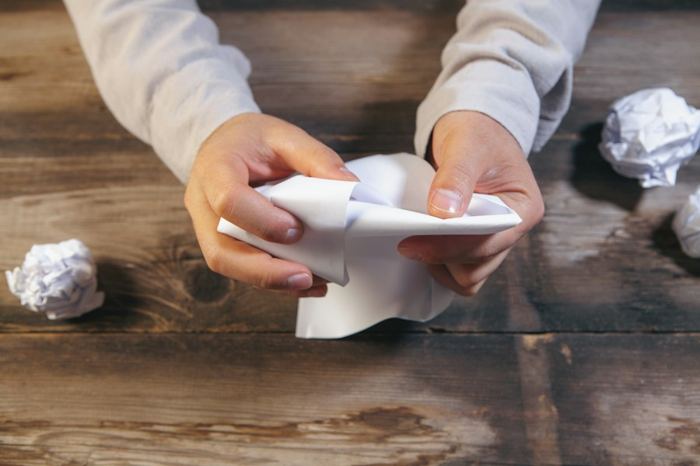 Des mains qui froissent une feuille de papier